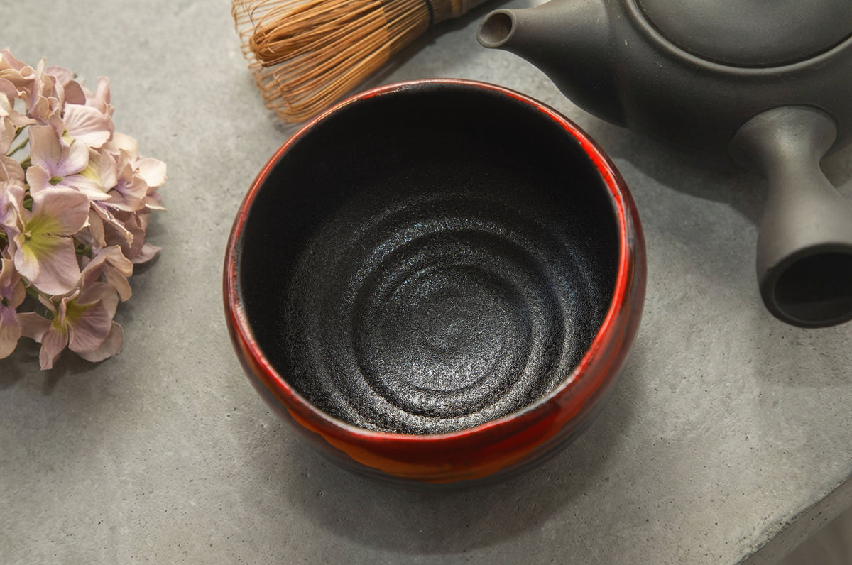 Red and black Mino-yaki matcha bowl with bamboo whisk and teapot