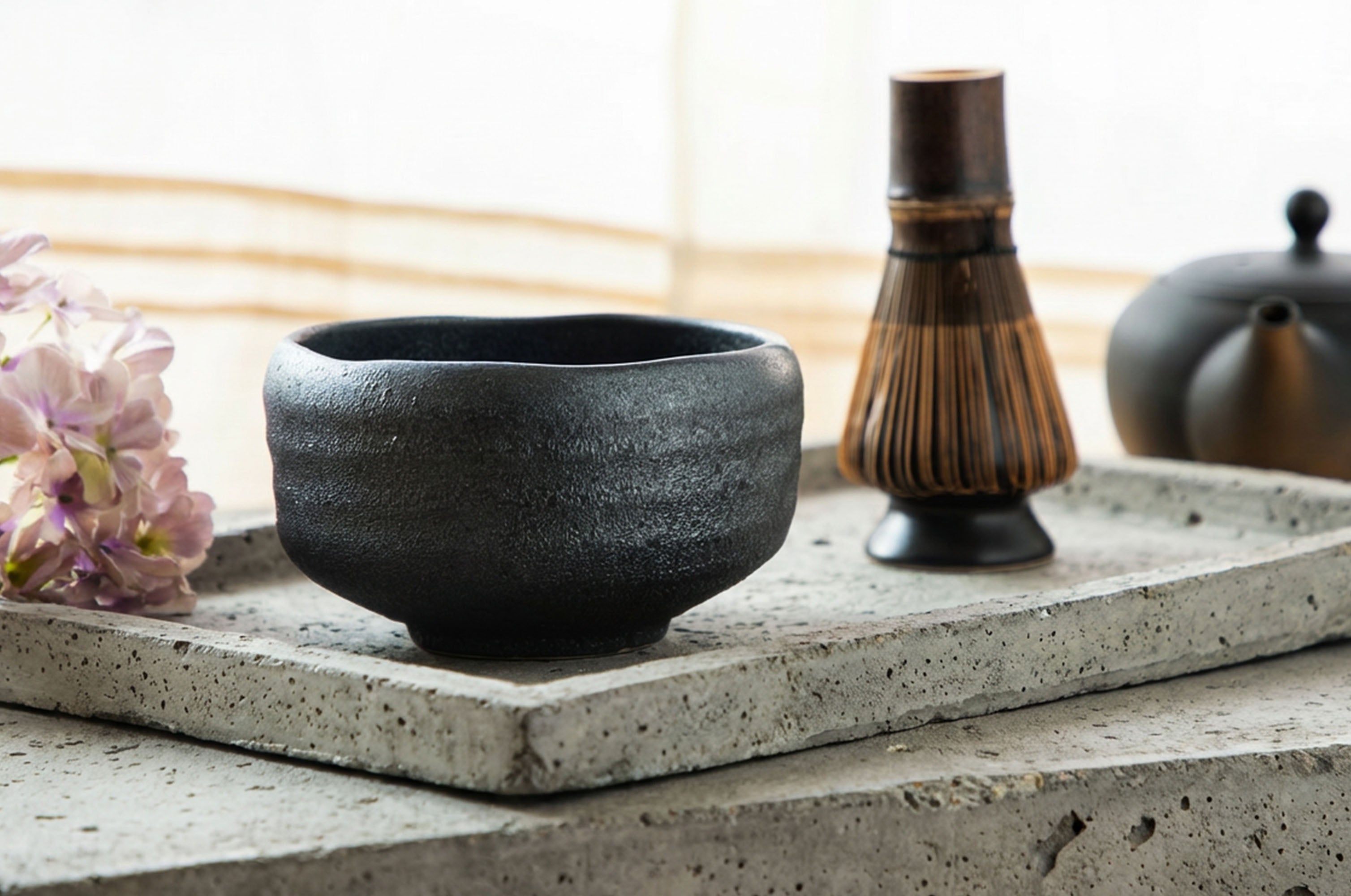 Japanese ceramic matcha bowl with a whisk and teapot in the background