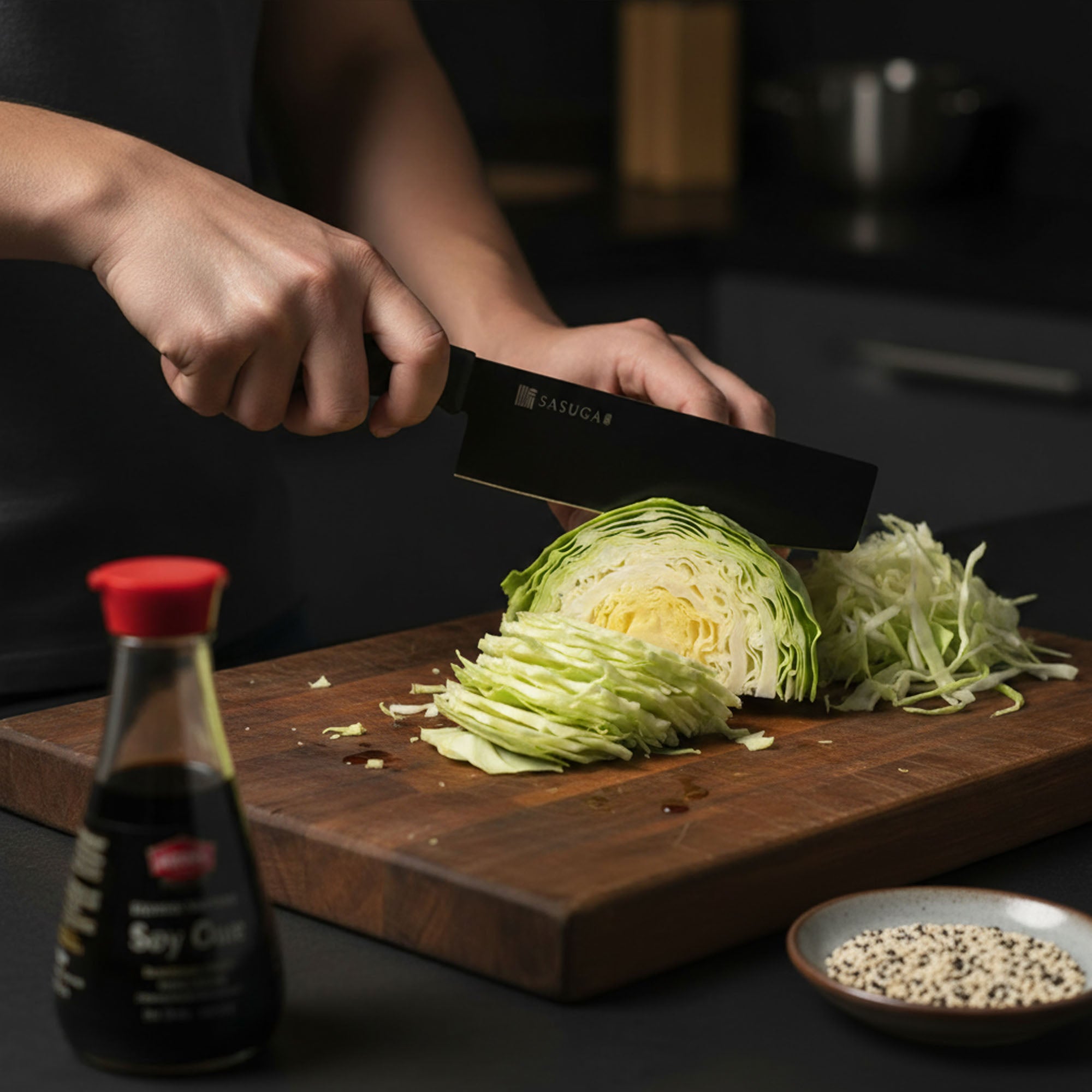 Person slicing cabbage on a wooden cutting board with a bottle of soy sauce and a bowl of spices in the foreground.