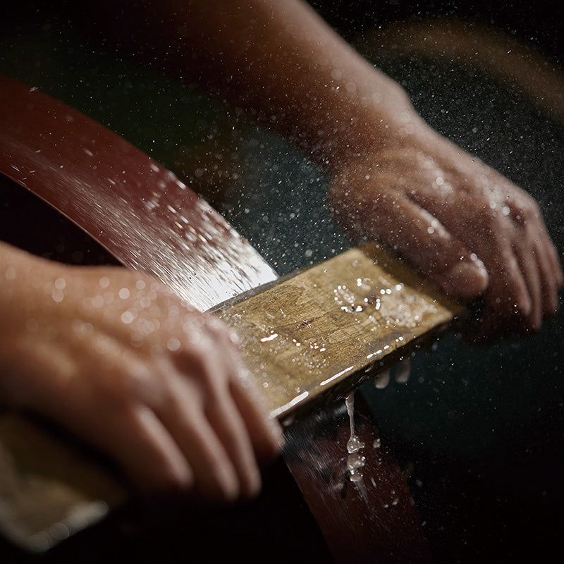 Person sharpening a blade on a whetstone with water droplets visible